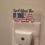 Frosted acrylic night light with a "God Bless the USA" American flag design, plugged into a wall outlet