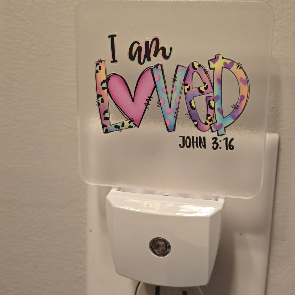 Frosted acrylic night light with a colorful heart and leopard print "I am Loved, John 3:16" design, plugged into a wall outlet
