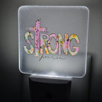 Frosted acrylic night light with a pink floral "She is Strong" cross design, glowing in a dark room