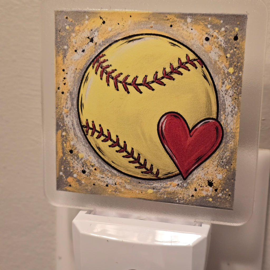 Frosted acrylic night light with a yellow softball and red heart design, plugged into a wall outlet