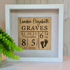 A personalized birth announcement shadow box with the name, birth date, weight, and length of a baby. The box is framed and displays this information on a wooden panel with a white background, accompanied by a silhouette of a foot.