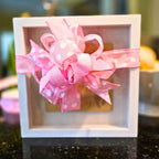 A personalized birth announcement shadow box with the name, birth date, weight, and length of a baby. The box is framed and displays this information on a wooden panel with a white background, accompanied by a silhouette of a foot. 
