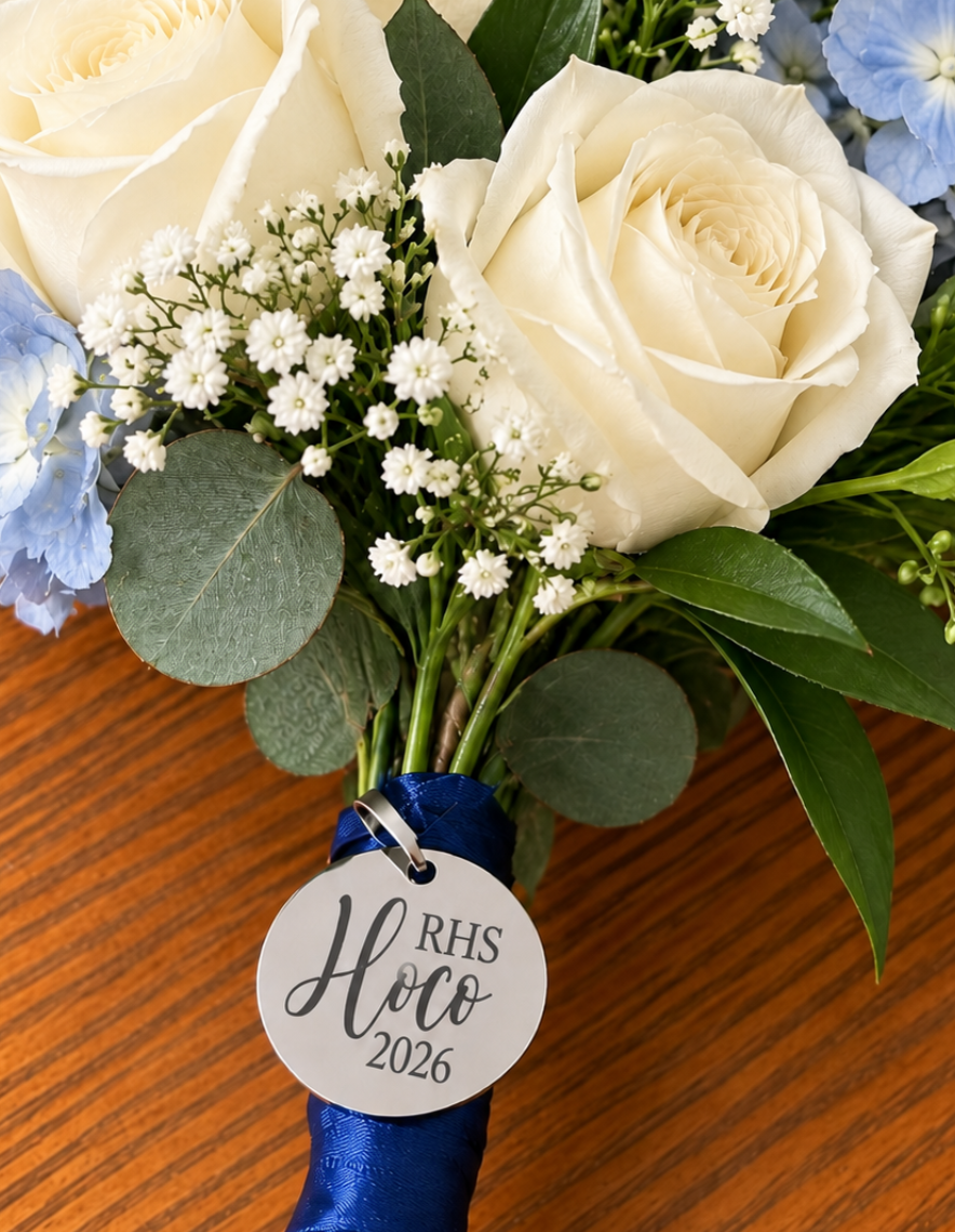 A close-up of a floral bouquet with blue ribbon  wrapped 'RHS HOCO 2026'. Laser engraved in Dothan, Alabama by Rise and Shine Gifts. Keepsake Homecoming Flower Charm.