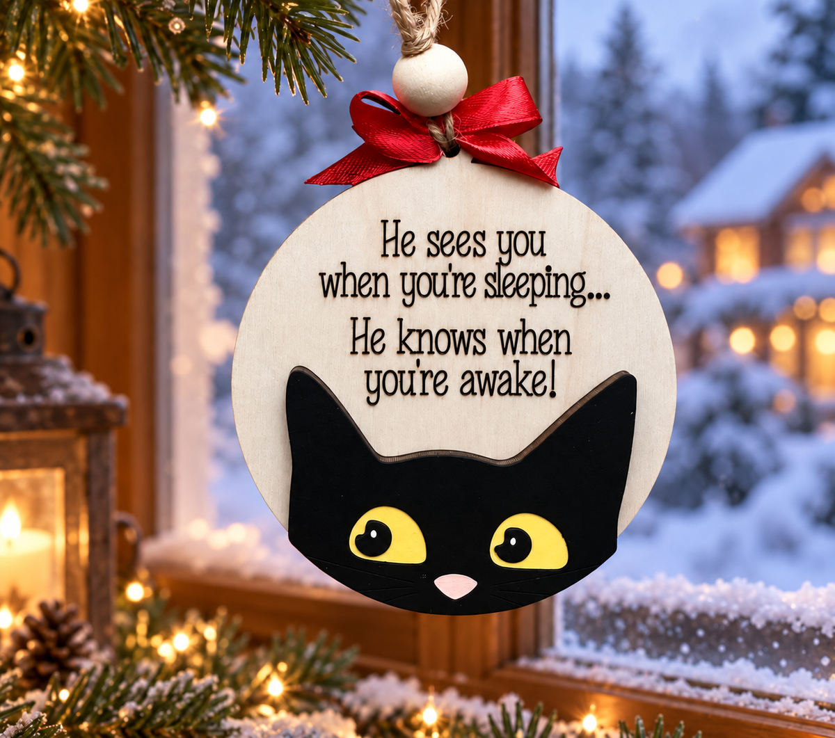 Black cat Christmas ornament with red bow hanging in a snowy winter window, cut by Rise and Shine Gifts in Dothan, Alabama OR-030