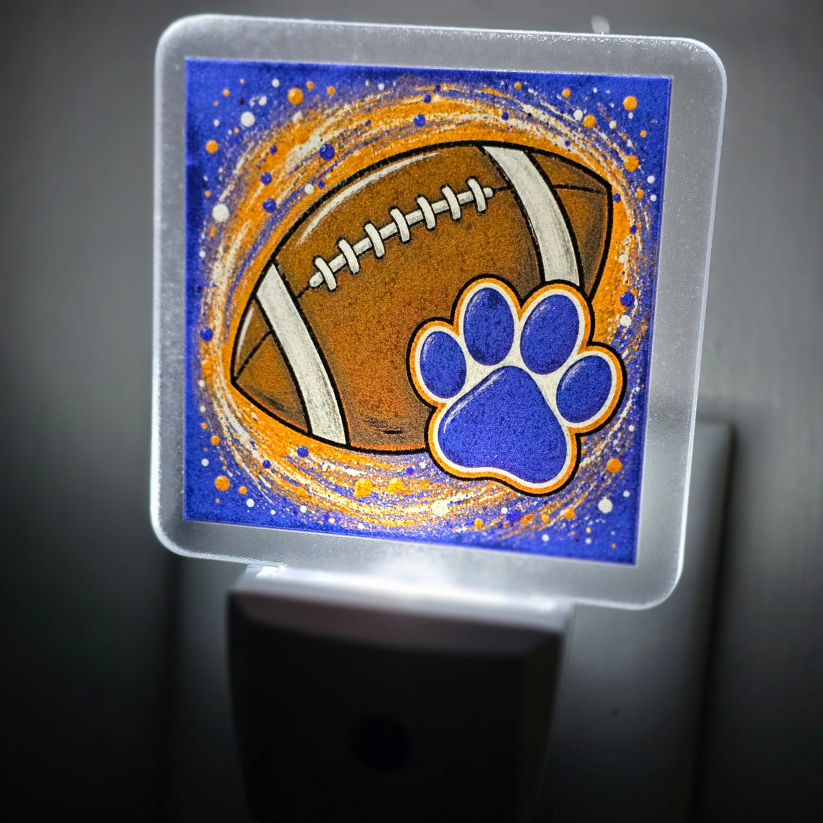 Frosted acrylic night light with a football and blue paw print on a blue and orange background, glowing in a dark room