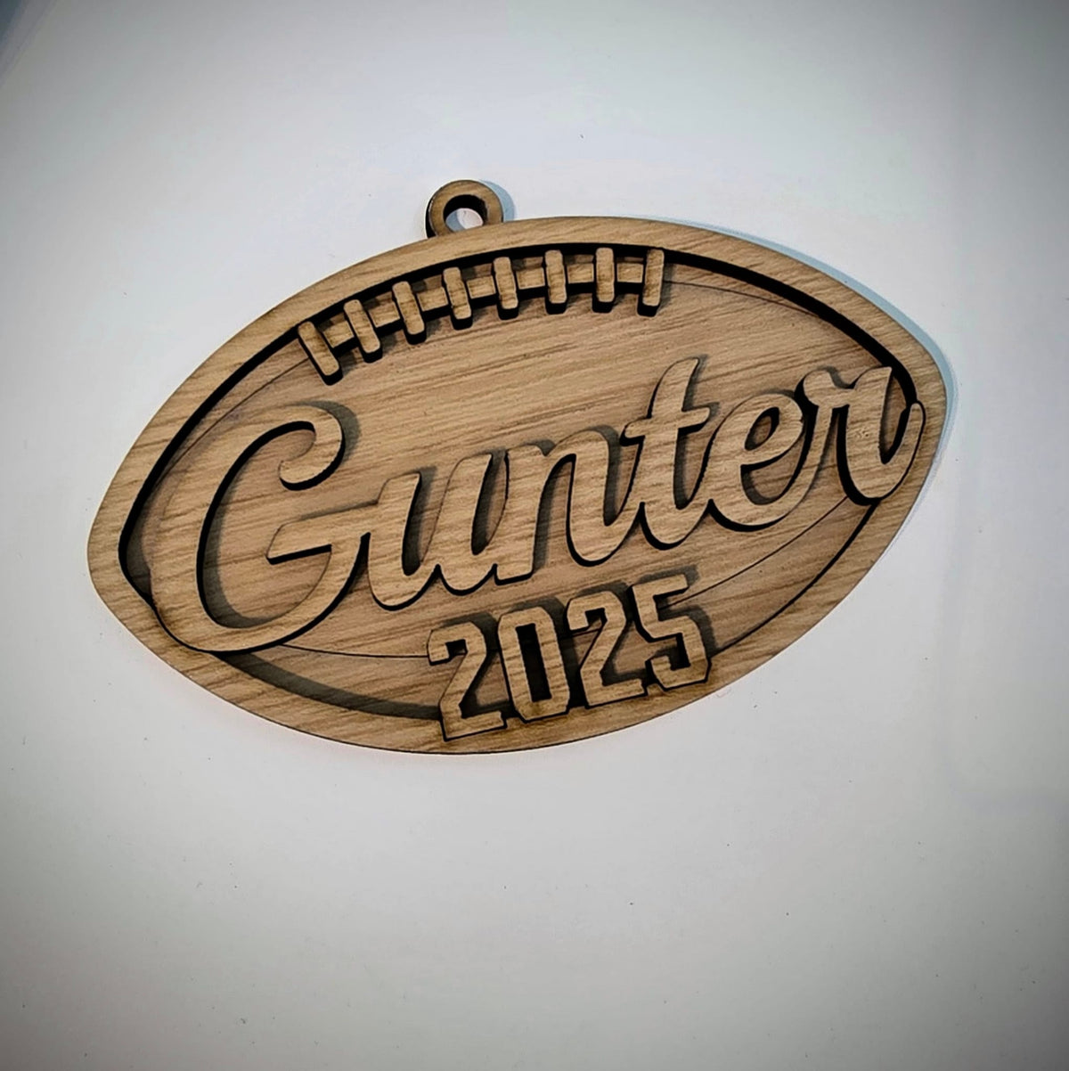Close-up of personalized football name and year layered wood ornament showing raised laces and letters, cut by Rise and Shine Gifts in Dothan, Alabama OR-034