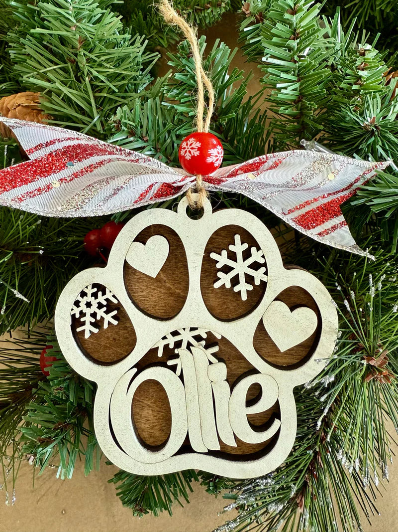 Handcrafted, personalized, Decorative Christmas ornament with paw print design and  customized pet name: 'Ollie' on a tree. 