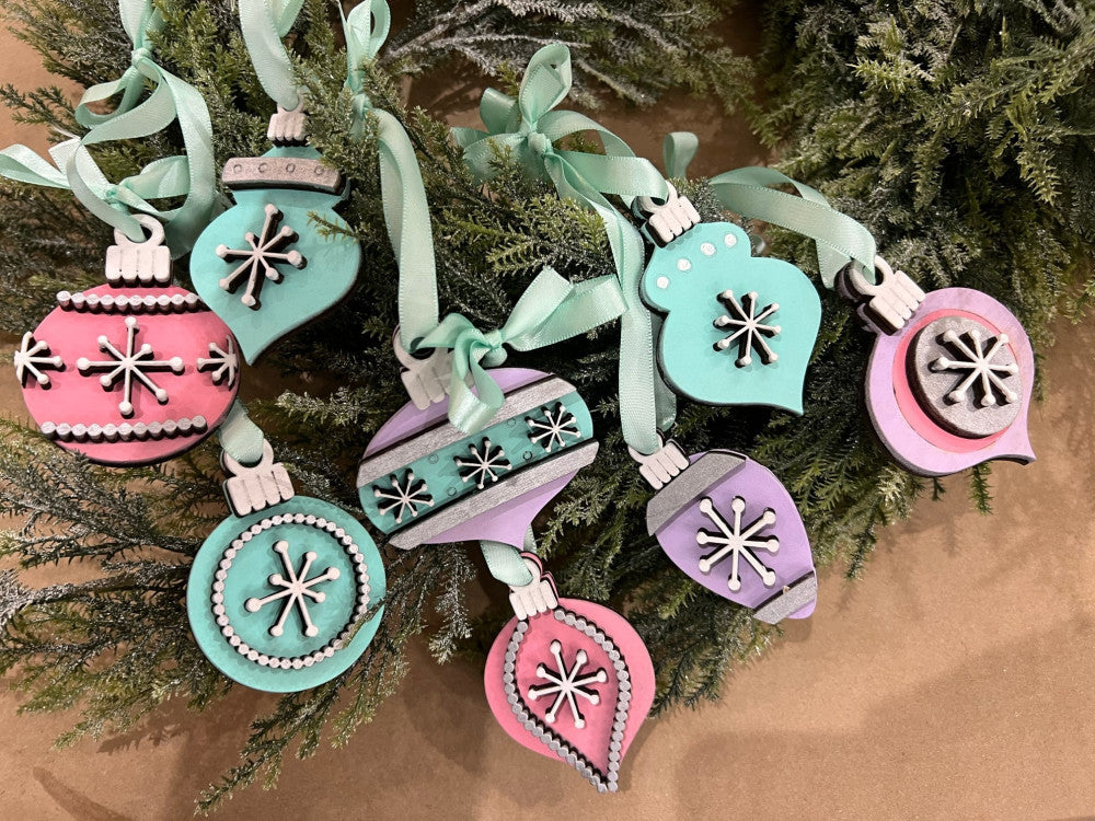 Set of eight retro-style layered wooden Christmas ornaments by Rise and Shine Gifts, shown with greenery and mint ribbons. DIY paint kit for Take & Make, craft parties, and pop-up events in Dothan, Alabama