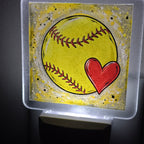 Frosted acrylic night light with a yellow softball and red heart design, glowing in a dark room.  UV-printed by Rise and Shine Gifts in Dothan, Alabama.