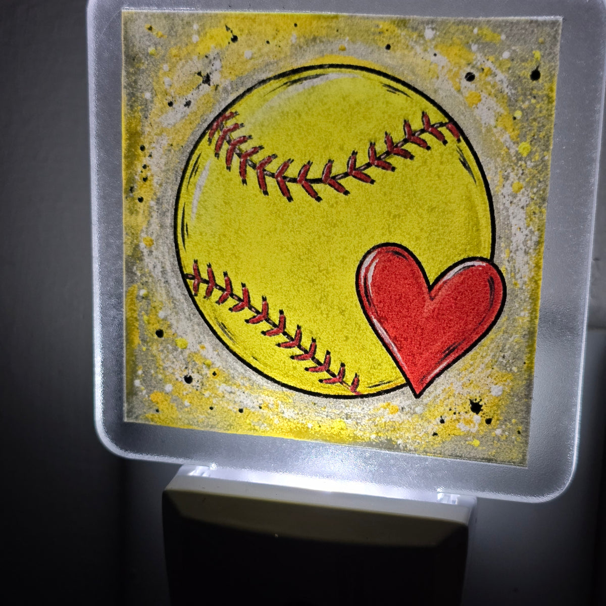 Frosted acrylic night light with a yellow softball and red heart design, glowing in a dark room.  UV-printed by Rise and Shine Gifts in Dothan, Alabama.